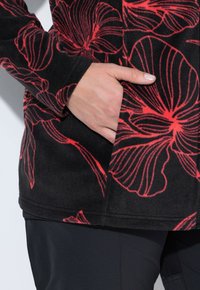 Giacca in pile nera con grande motivo floreale rosso, dotata di tasca laterale. Tessuto liscio, maniche lunghe e design dal taglio rilassato.