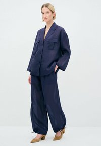 Completo in lino blu navy con camicia a vestibilità ampia dotata di due tasche frontali e pantaloni abbinati con polsini elasticizzati e dettagli legati.