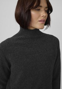 Tumši pelēks turtlenecks džemperis ar mīkstu, ribotu adījumu, piedāvā augstu apkakli un brīvu piegriezumu.