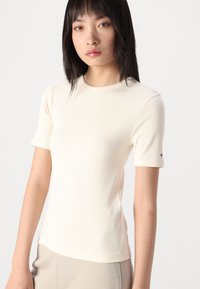 Geribbelde, crèmekleurige top met korte mouwen en een ronde hals. Beschikt over een subtiele logo-accent op de mouw en een slim fit ontwerp.