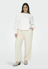 Felpa bianca con dettagli in occhiello sulle maniche, abbinata a pantaloni a gamba larga di un beige chiaro e stivali alla caviglia color taupe. Texture lisce in tutto l'outfit.