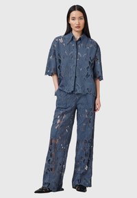 Set in pizzo blu profondo composto da top e pantaloni con motivi a farfalla, maniche corte e design a gamba larga, con dettagli a taglio e bordi scallop.