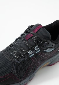 Chaussure de sport noire avec dessus en maille texturée, détails gris foncé, accents bordeaux et lacets réfléchissants, dotée d'une semelle coussinée.