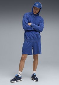 Blå pullover hoodie med känguruficka, ihop med matchande blå shorts. Sneakers är i mörkblått och svart med accentfärger och snörning.