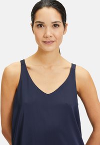 Granatowy top bez rękawów z dekoltem w kształcie litery V oraz cienkimi ramiączkami, charakteryzujący się gładką teksturą i luźnym krojem. Brak widocznych wzorów lub elementów metalowych.