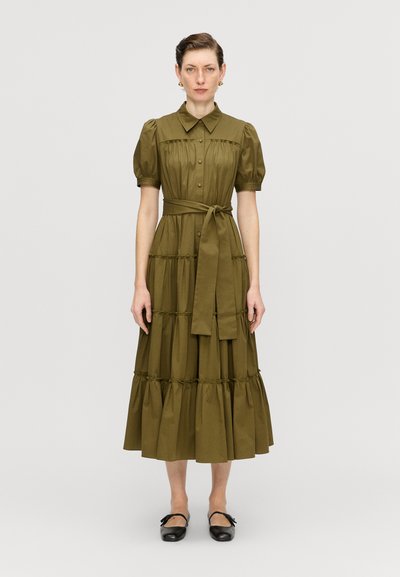 Robe vert olive, longueur genoux, avec un col, des manches courtes bouffantes, un front boutonné et une taille nouée. Présente des volants superposés et froncés.