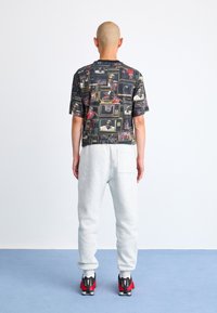 Kortærmet sort t-shirt med et farverigt grafisk print, parret med grå sweatpants og sorte/røde sneakers. Glat stof, afslappet pasform.