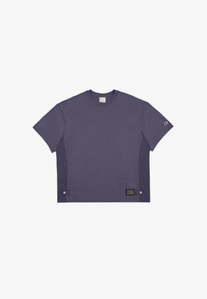 Fioletowa koszulka z krótkim rękawem wykonana z bawełny. Posiada okrągły dekolt, boczne panele oraz metkę z tekstem po lewej dolnej stronie.