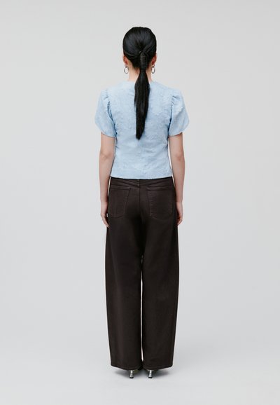 Blusa azzurro chiaro con texture e maniche a sbuffo, abbinata a pantaloni beige a vita alta a gamba larga. Orecchini a cerchio in metallo completano il look.
