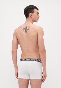 Fehér boxer alsónadrág fekete "justcavalli" derékpánttal. Az anyag simának tűnik. Egy dekoratív tetoválás látható a hátsó részen.