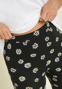 Svarta leggings med en prästkrage-mönster med vita blad och gula mitten. Elastisk midja, slät textur, åtsittande form.