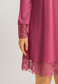 Abito rosa con maniche lunghe. Il bordo in pizzo sui polsini e sull'orlo presenta motivi floreali. Tessuto liscio con una leggera lucentezza.