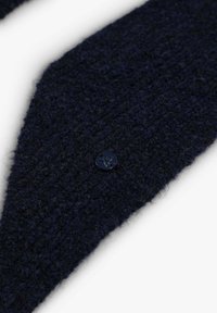 Bufanda de lana azul marino con un acabado texturizado. Presenta un gran botón oscuro como detalle. Cortada en forma triangular.