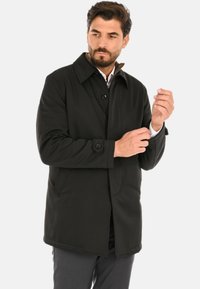 Trench nero con colletto classico, chiusura con bottoni e tasche laterali. Tessuto liscio con una vestibilità sartoriale.