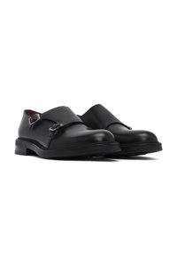 Schwarze Lederschuhe mit elegantem Design, ausgestattet mit einem Schnallenriemen und glatter Oberfläche. Niedriger Absatz und runde Zehenform, die minimalistische Akzente hervorhebt.