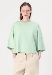 Menta zelena oversized pamučna majica s okruglim vratom i kratkim širokim rukavima, uparen s bež hlačama visokog struka s detaljem gumba.