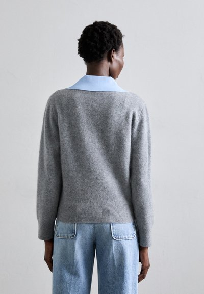 Suéter de punto gris con un cuello azul claro, que presenta un corte relajado, dobladillo acanalado y textura suave; combinado con jeans azul de cintura alta.