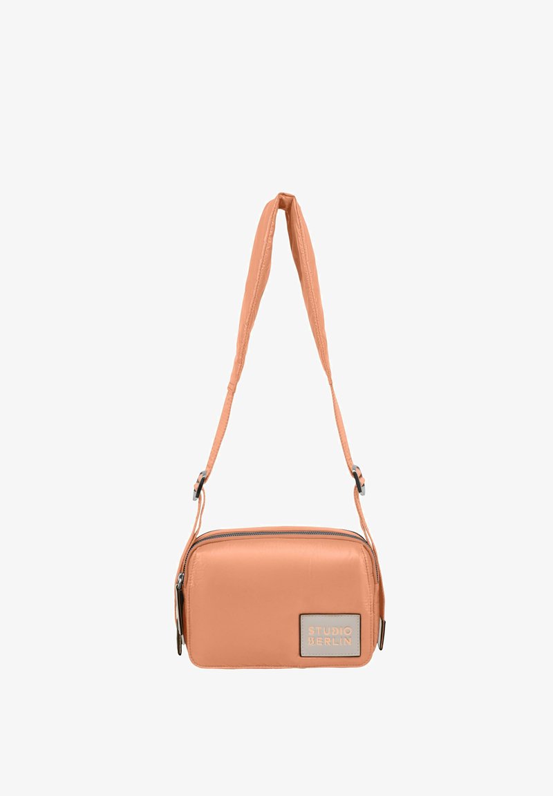 Prostokątna torba crossbody w kolorze brzoskwiniowym, wykonana z gładkiej sztucznej skóry, z zamkiem błyskawicznym i regulowanym paskiem. Posiada plakietkę z logo.