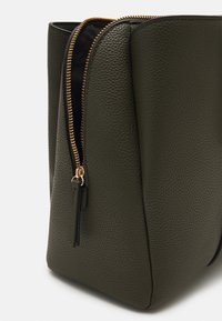 Pochette en simili cuir texturé vert olive avec une fermeture éclair dorée, offrant un intérieur spacieux et un design angulaire.