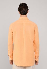 Lange mouwen shirt van lichtoranje linnen. Voorzien van een button-down kraag, een subtiele rugplooi en knopen op de manchetten. Gladde textuur.
