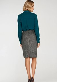 Turkusowa bluzka z długim rękawem w połączeniu z dopasowaną szaro-cętkowaną spódnicą ołówkową z tylnym zamkiem. Gładki materiał o prostym wzorze.