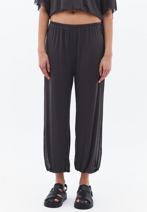 Pantalones cortos de color gris oscuro, ligeros, con cintura elástica e inserciones laterales de malla. Combinados con sandalias negras de tiras. Textura suave.