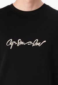 T-shirt en coton noir avec un logo en script blanc bien en évidence sur la poitrine. L'encolure est de style classique à col rond.
