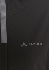 Svart jacka av slät tyg, med en grå reflekterande rand och en tryckt "VAUDE"-logotyp på nedre högra sidan.