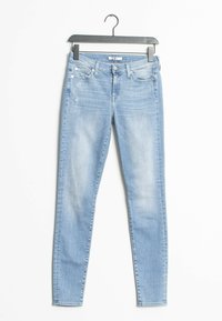 Jeans ajustados de color azul claro con una textura desgastada, diseño básico de cinco bolsillos, sutiles arrugas y cierre de botón. Colgados de una percha de metal negro.