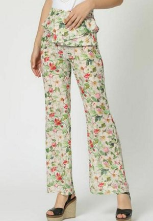 Pantalones con estampado floral sobre un fondo verde claro, que presentan una cinturilla con volantes y piernas anchas, combinados con sandalias de cuña negras.