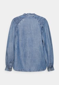 Camisa de ganga com colarinho franzido e design de ombros plissados. Cor azul clara com mangas longas e punhos abotoados. Textura suave.
