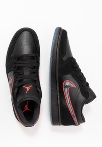 Baskets en cuir noir avec des accents rouges. Elles présentent un bout perforé, un swoosh texturé noir et rouge, et une semelle translucide.
