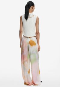 Top bianco senza maniche abbinato a pantaloni larghi a vita alta multicolori con motivo floreale, realizzati in un tessuto morbido e con una superficie liscia.