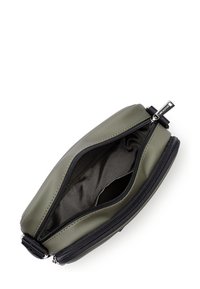 Pochette compatta di colore verde oliva con due scomparti neri con zip, parzialmente aperta per mostrare l'interno in morbido tessuto nero con una piccola tasca interna.