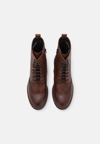 Bottines en cuir marron avec détails brogue, design à lacets, fermetures éclair latérales et bout arrondi. Semelle texturée pour une meilleure adhérence.