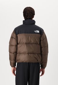 Geacă puf bărbătească de culoare maro, cu partea superioară neagră, având un guler înalt, manșete elastice și un logo pe spate. Textură moale, matlasată.