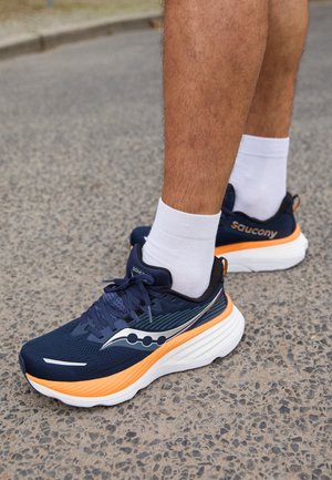 Scarpe da corsa navy con accenti arancioni, tomaia in rete strutturata, suola intermedia spessa bianca e colletto imbottito. Indossate con calzini bianchi alla caviglia.