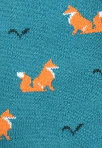 Pleteni tekstil v barvi modrozelenih tonov z raztresenimi oranžnimi lisicami z belimi poudarki in majhnimi črnimi ptiči, ki ustvarjajo igriv vzorec.