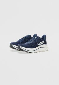 Scarpe da corsa navy con tomaia in rete, logo HOKA bianco, collare imbottito e suola spessa e ammortizzata con una suola esterna nera e testurizzata.