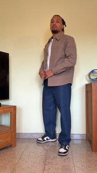 Camicia marrone a maniche lunghe sopra una t-shirt bianca, abbinata a jeans blu a gamba dritta e sneakers nere e bianche. Design semplice, dettagli minimi.