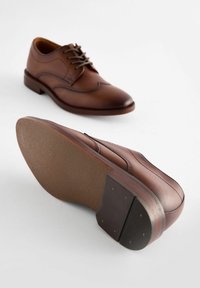 Chaussures habillées en cuir marron avec un bout arrondi, des accents cousus et des lacets. Semelle en caoutchouc texturé avec un motif discret et des détails au niveau du talon.