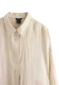 Beige linned skjorte med krave, frontknapper, lange ærmer og en afslappet pasform. Materialet ser let og struktureret ud.