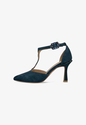 Marineblauwe suede hoge hakken met een puntige neus en een T-bandontwerp. Voorzien van een decoratieve edelsteensluiting op de enkelband.