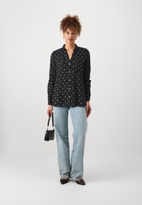 Svart skjorte med hvite prikker, lange ermer og knappestolpe, kombinert med lyseblå høyt liv jeans og svarte spisse sko.