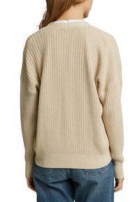 Beige gebreide trui met een getextureerd ribpatroon, met een wijde halslijn en een ontspannen pasvorm. Gecombineerd met hooggeribde blauwe jeans.