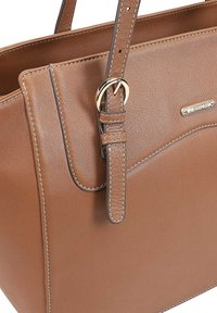 Bruine leren handtas met een gladde textuur, voorzien van een gouden hardware accent en contrasterende stiksels langs de randen.