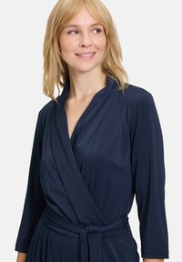 Abito avvolgente blu navy con maniche lunghe, tessuto morbido, cintura in vita e scollatura a V. Caratterizzato da una vestibilità rilassata e un drappeggio sottile.