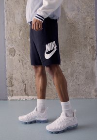 Nike-shorts i marinblått med en stor vit logotyp, kombinerat med vita sneakers som har genomskinlig luftdämpning och texturerad detaljering på ovandelen.
