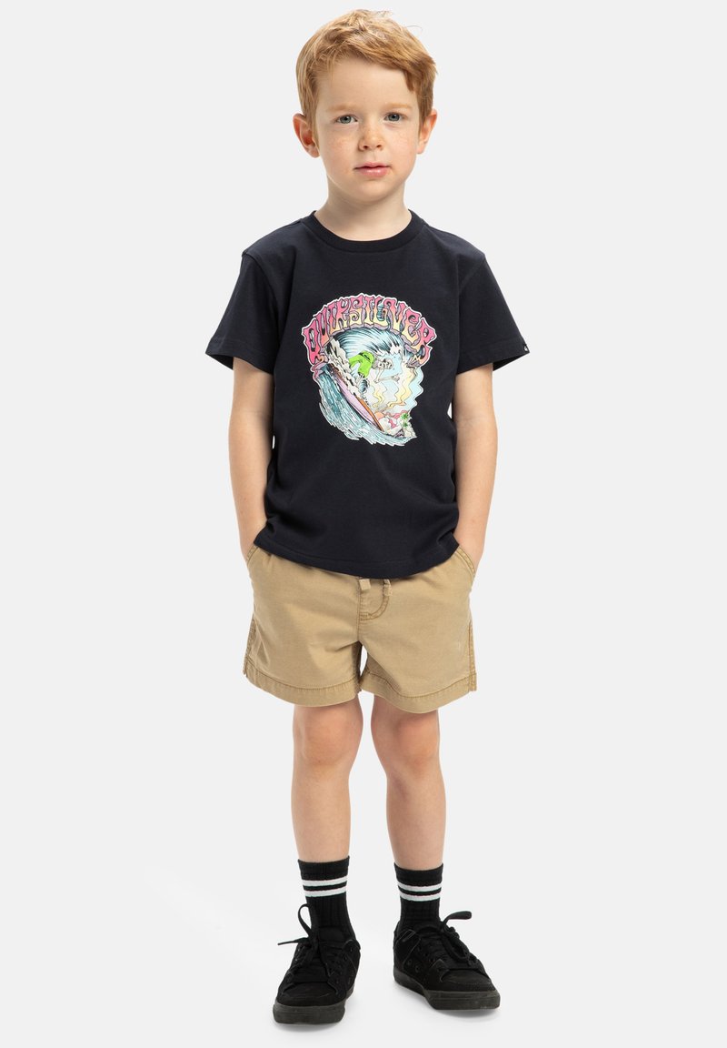 Svart bomullströja med färggrafik av vågor, tillsammans med bruna shorts. Barnet har på sig svarta skor och randiga svartvita strumpor.
