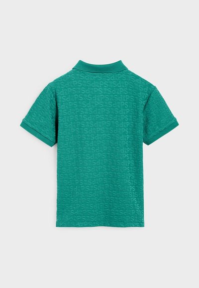Grön polo med en strukturerad mönster av upprepade bokstäver, ribbad krage och korta ärmar.